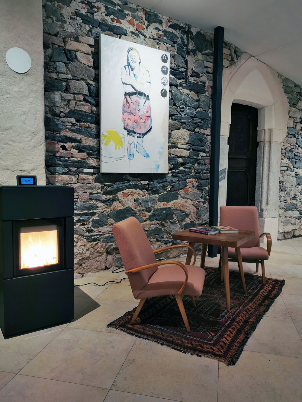 Cozy room with fireplace, two armchairs, table and artwork on a stone wall.