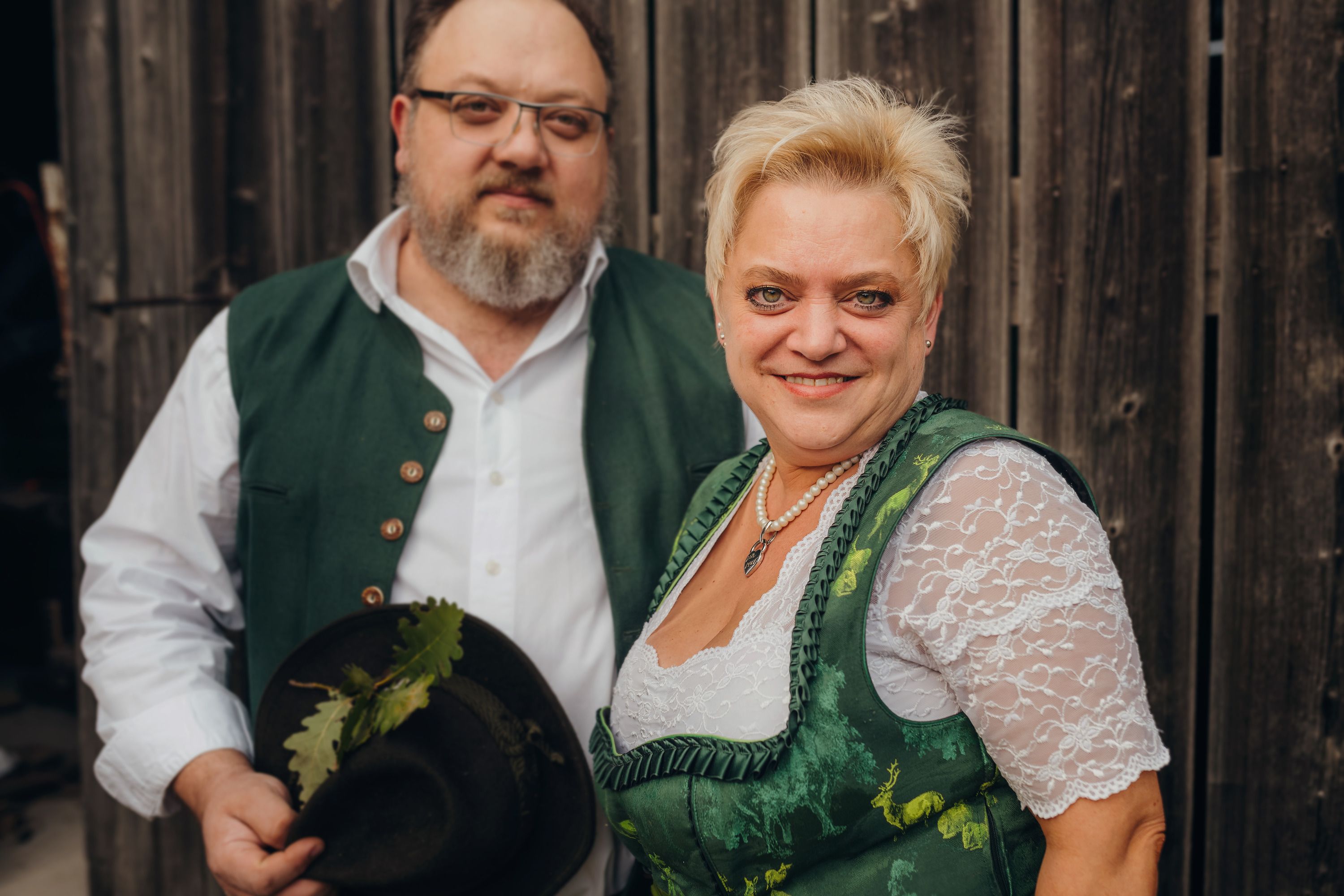 A man and a woman in traditional costume in front of a wooden wall.