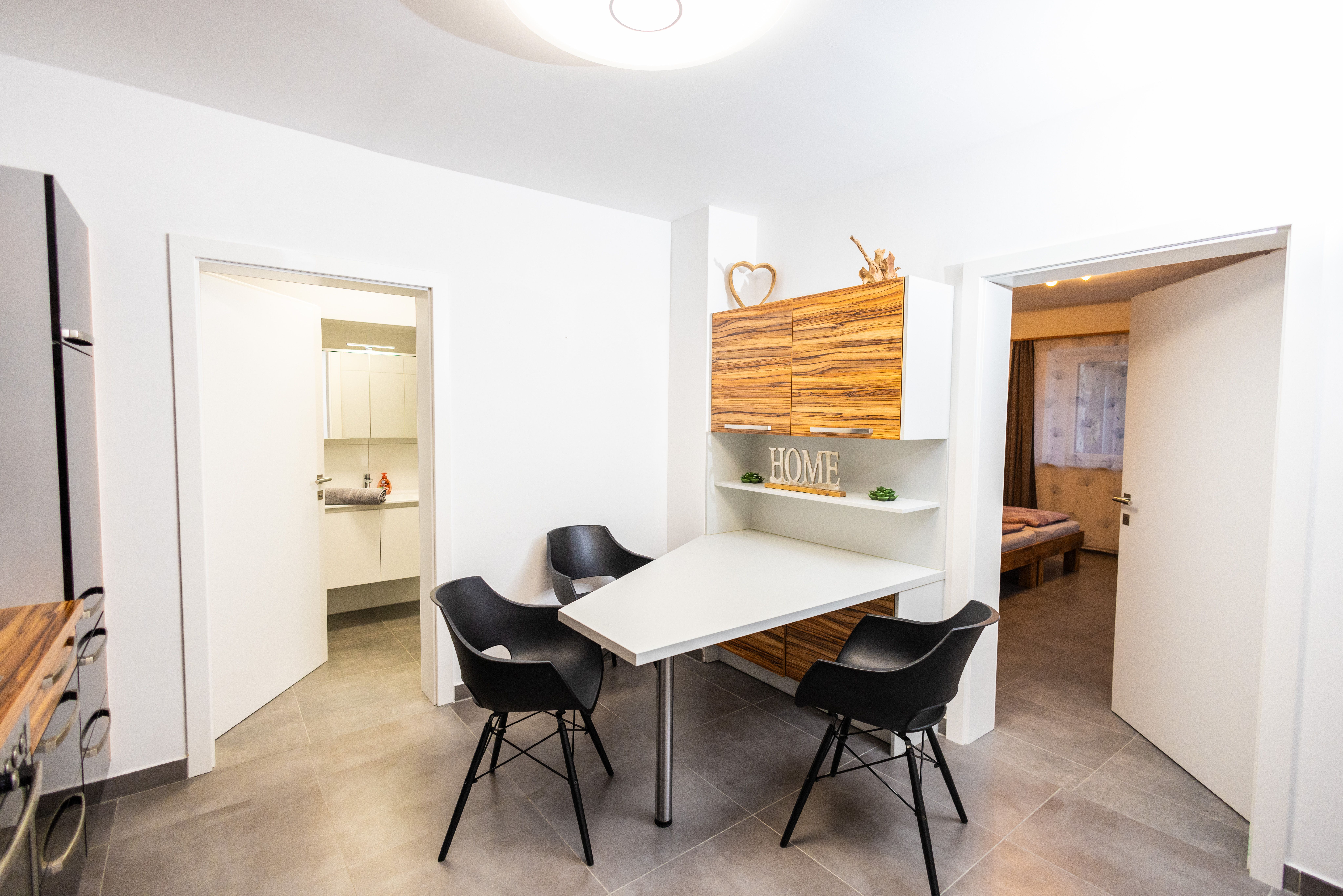 Modern dining area with table, black chairs and wooden cupboards.