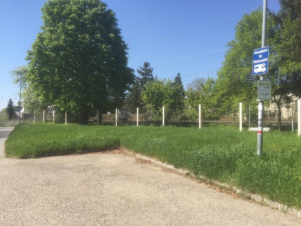 Caravan site with sign, surrounded by trees and grass.