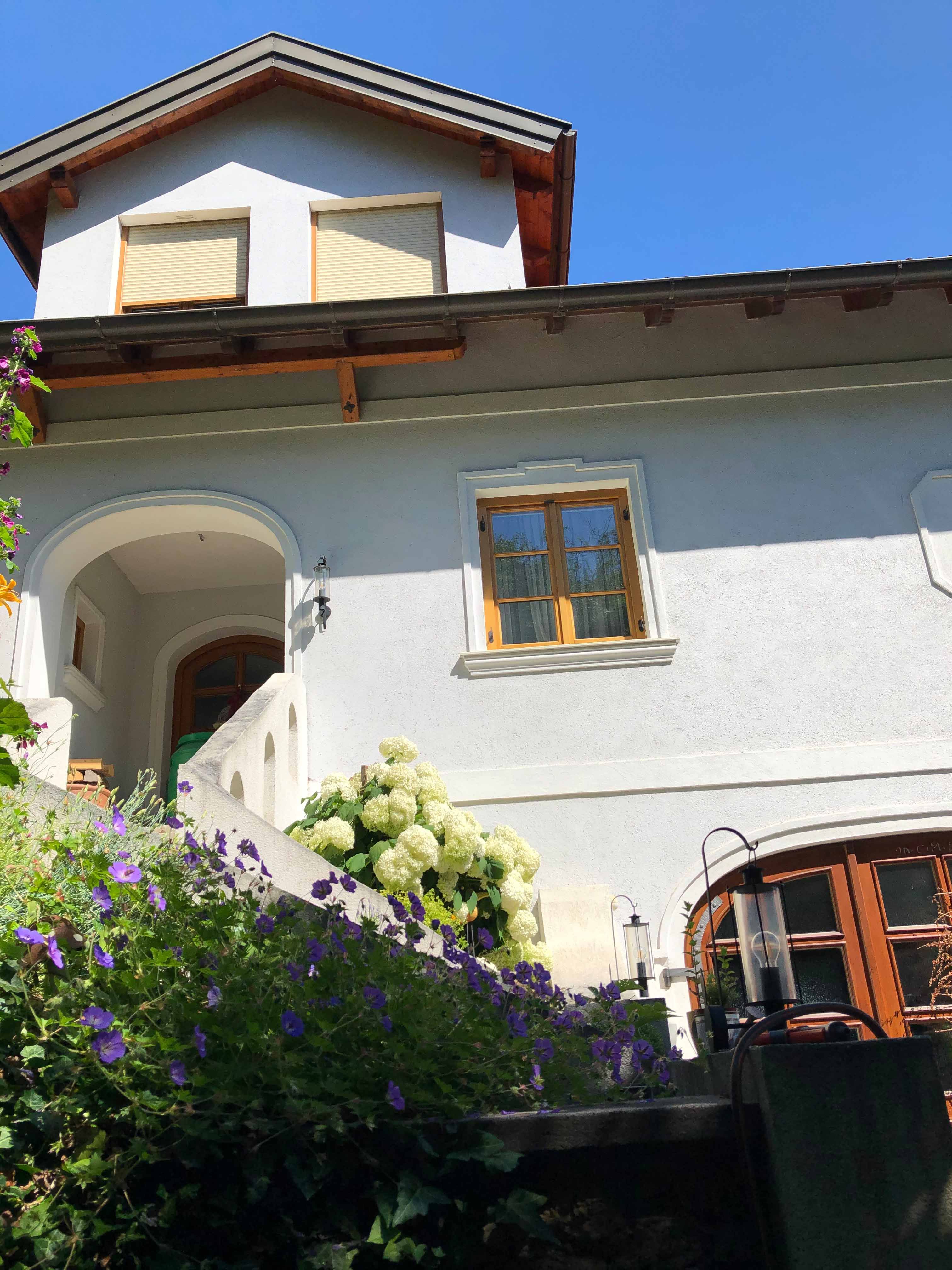 House with white walls, wooden roof and flowers in the foreground.