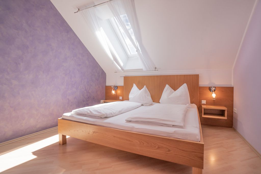 Bright bedroom with skylight, purple wall and wooden bed.