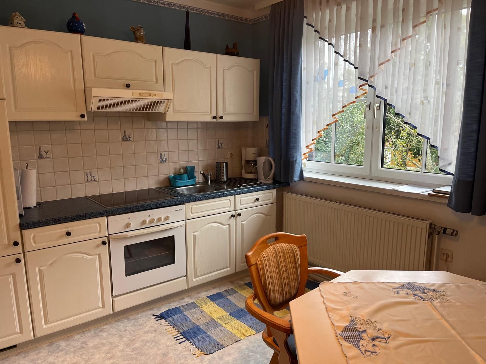 Kitchen with white cupboards, stove, sink and window with curtains.
