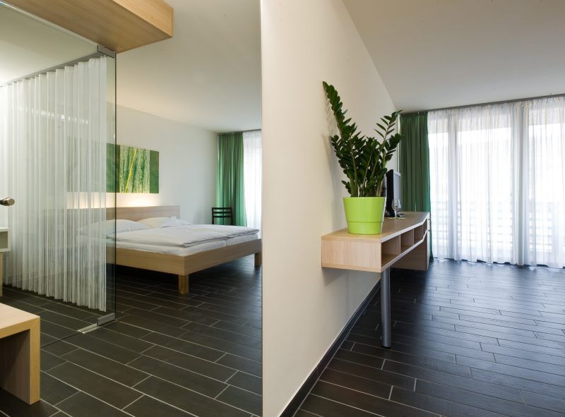 Modern hotel room with double bed, green curtain and houseplant.
