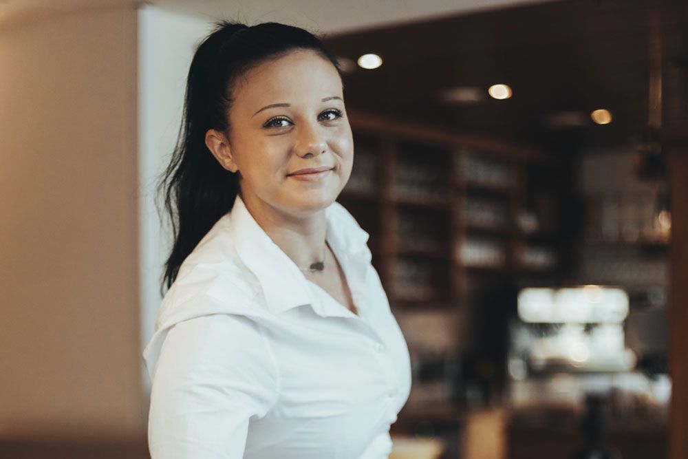 Woman in white shirt smiles into the camera, background blurred.