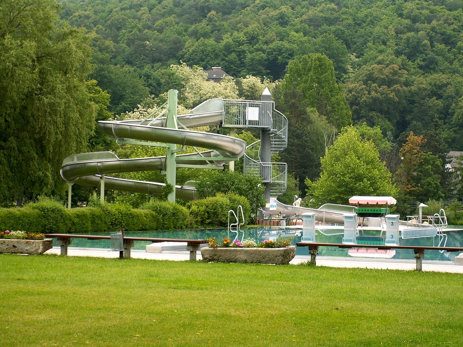 An outdoor pool with slide and pool, surrounded by trees.