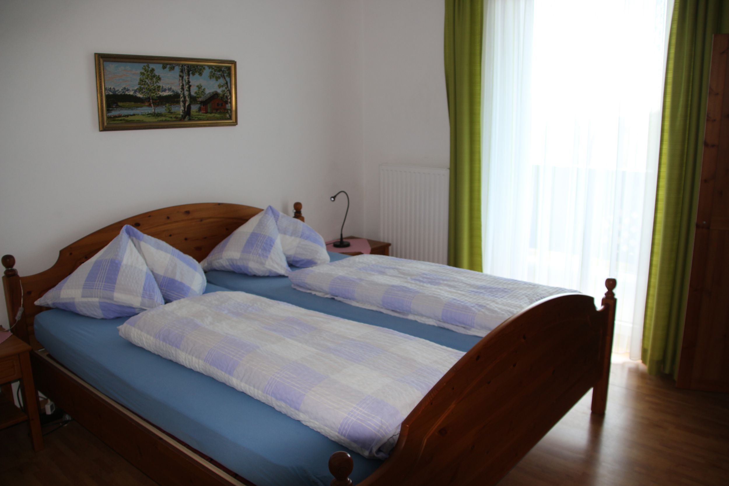 Double room with wooden bed, blue and white checkered bed linen, picture on the wall and green curtain.