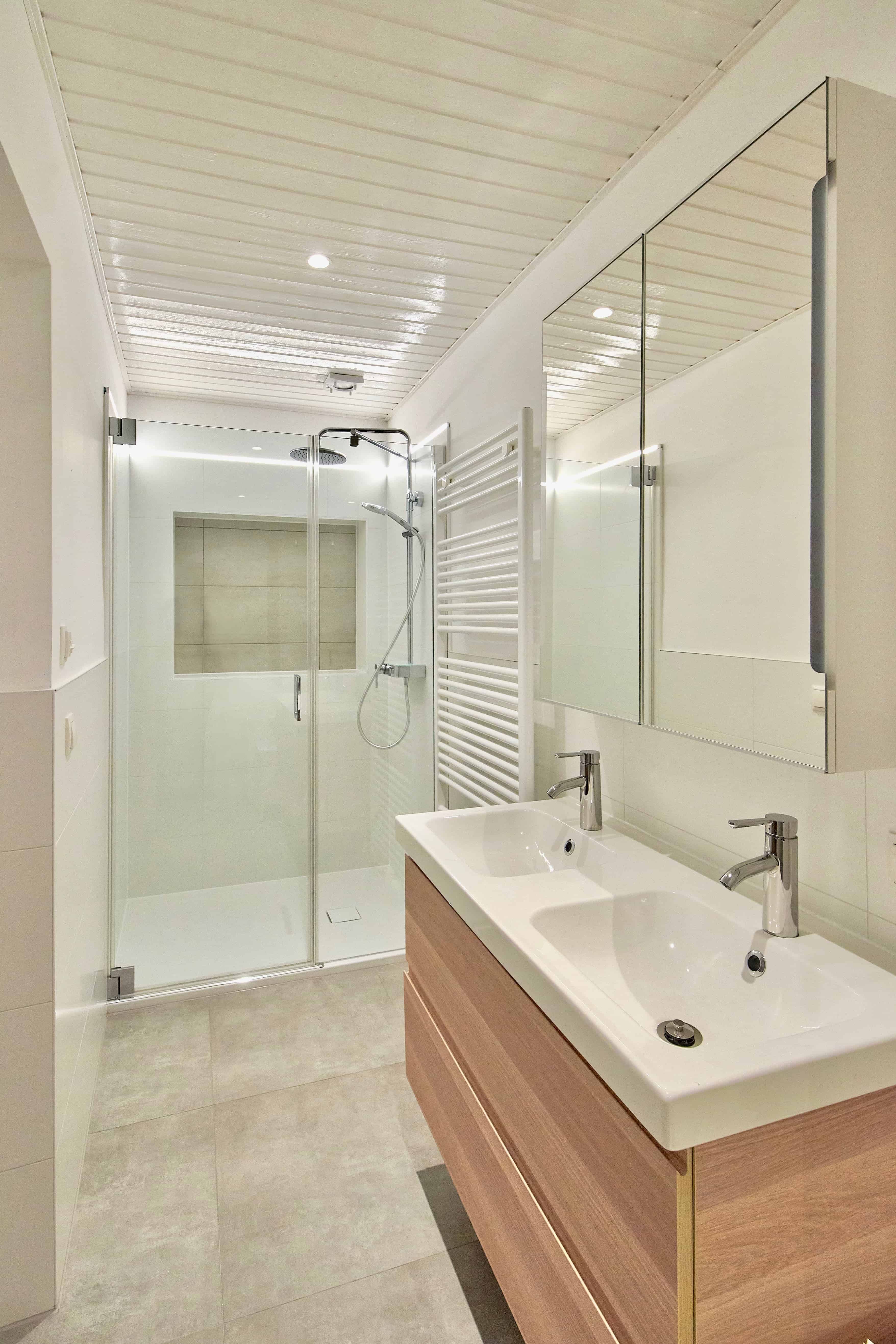 Modern bathroom with double washbasin, glass shower and towel radiator.