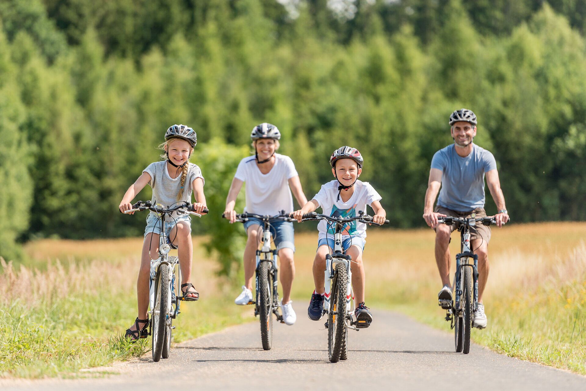 A happy family cycles together along a picturesque path surrounded by lush greenery and rolling hills. The sun shines in the blue sky and creates an inviting atmosphere for unforgettable experiences in nature.