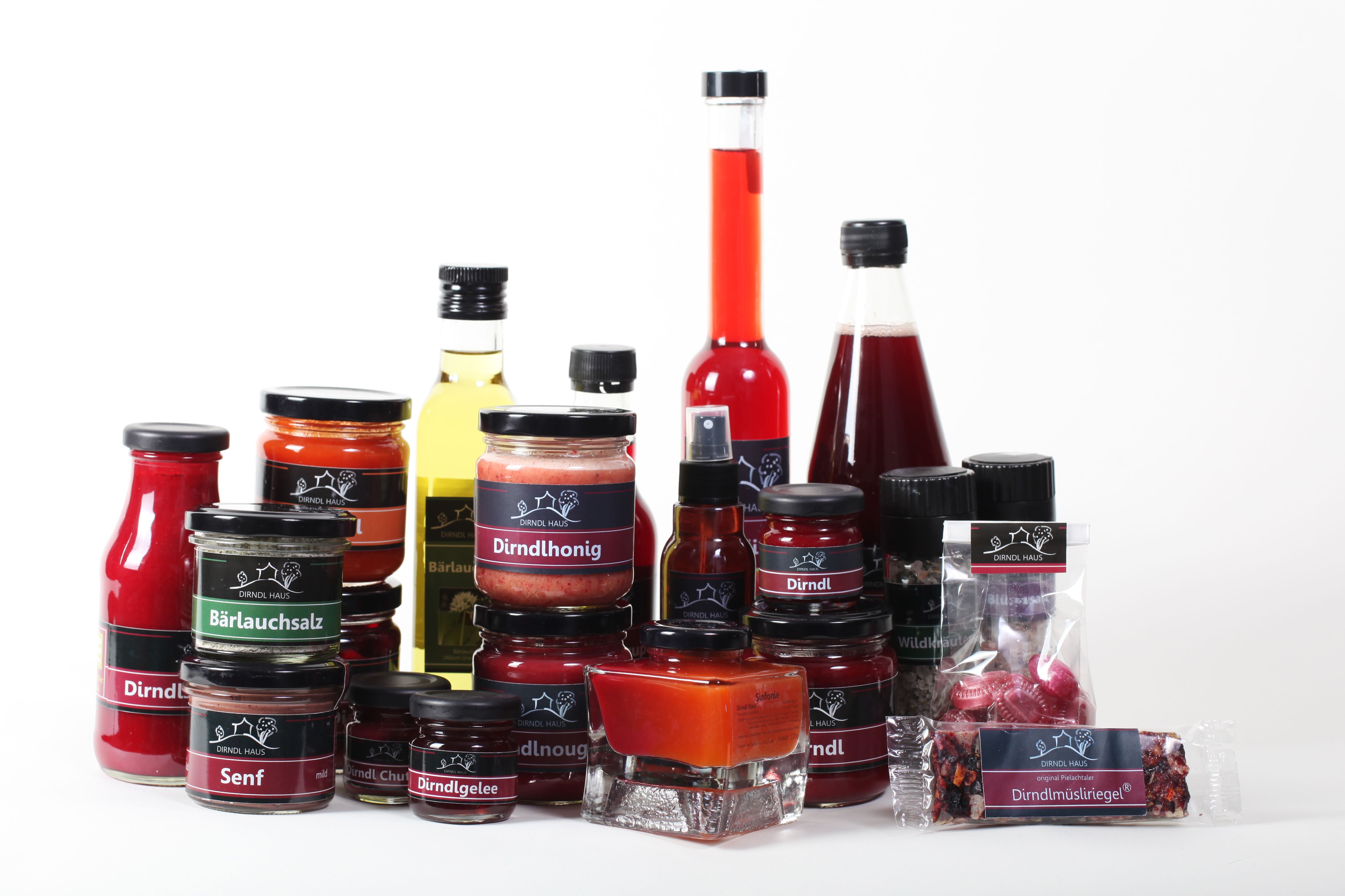 Various Dirndl Haus products, including honey, jelly, mustard and oil, on a white background.