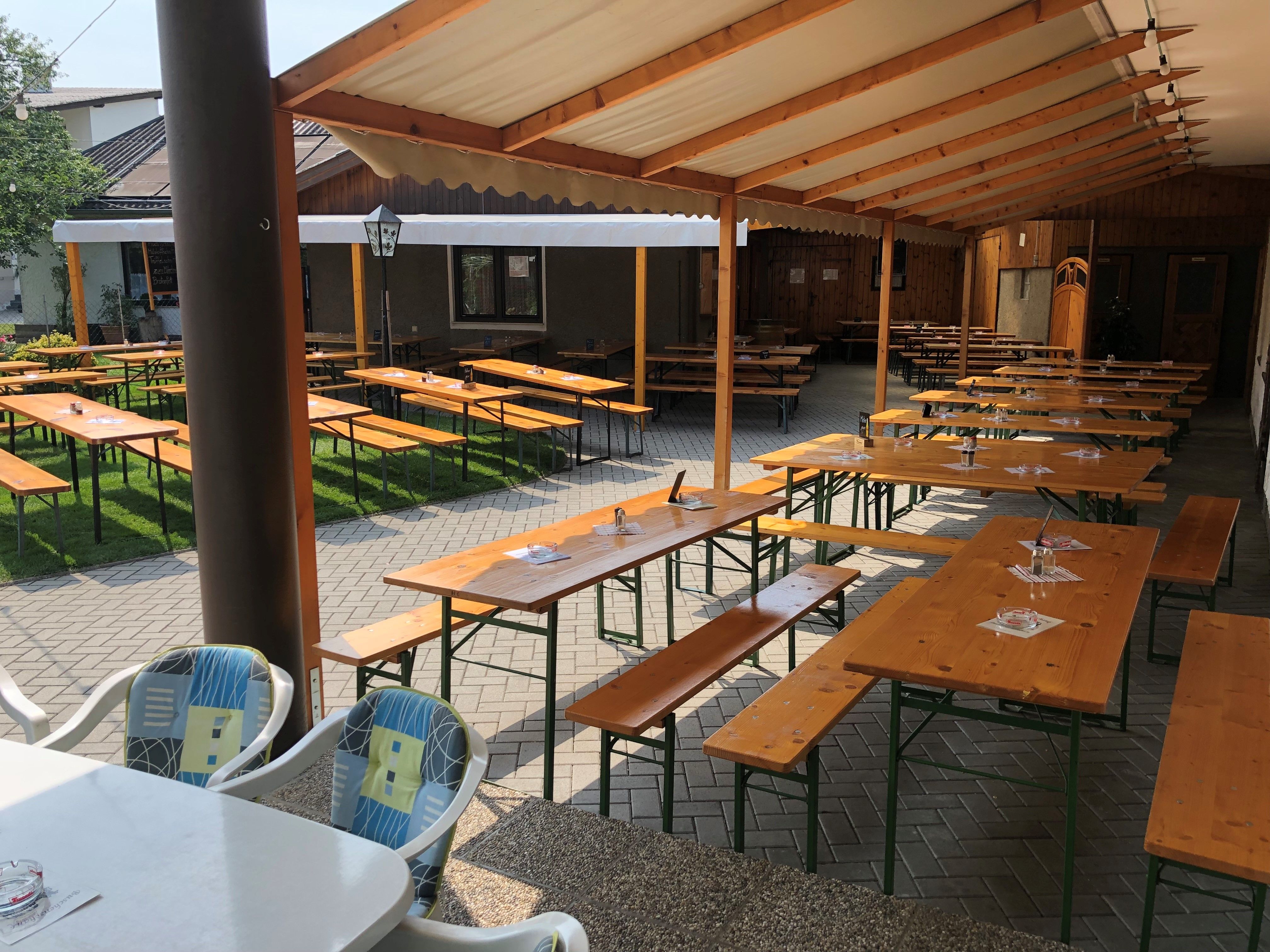 An empty wine tavern garden with wooden benches and tables under a covered area.
