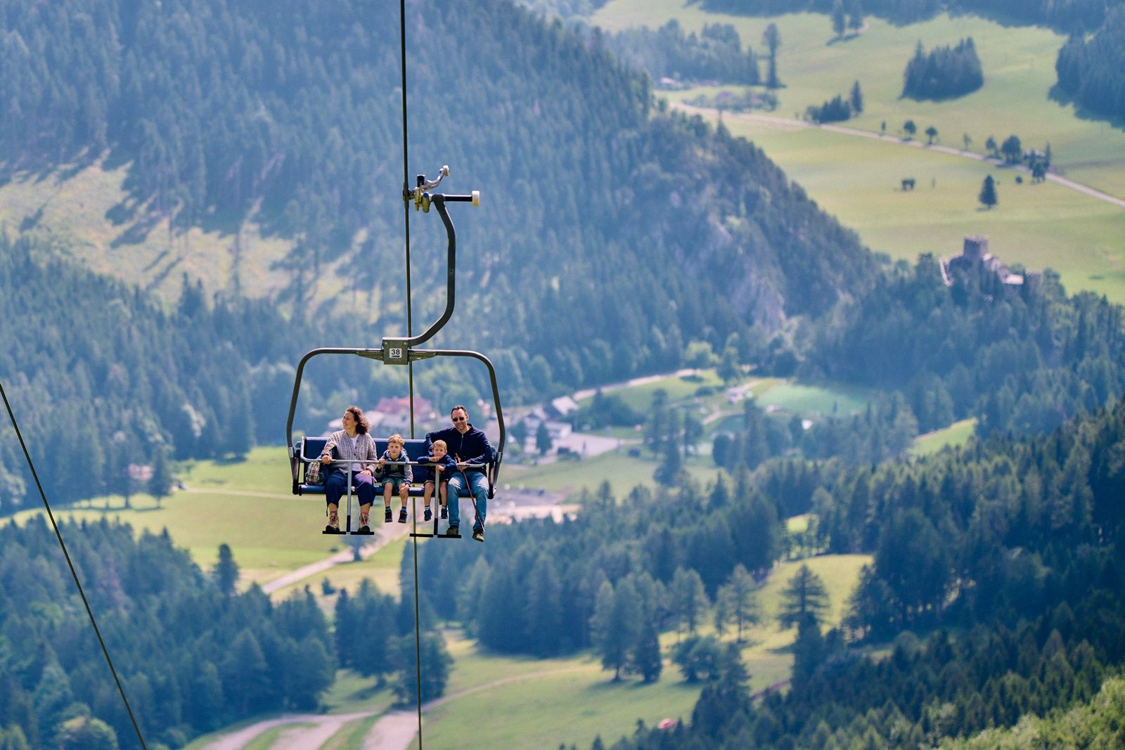 A family rides a chair lift over a green mountain landscape.