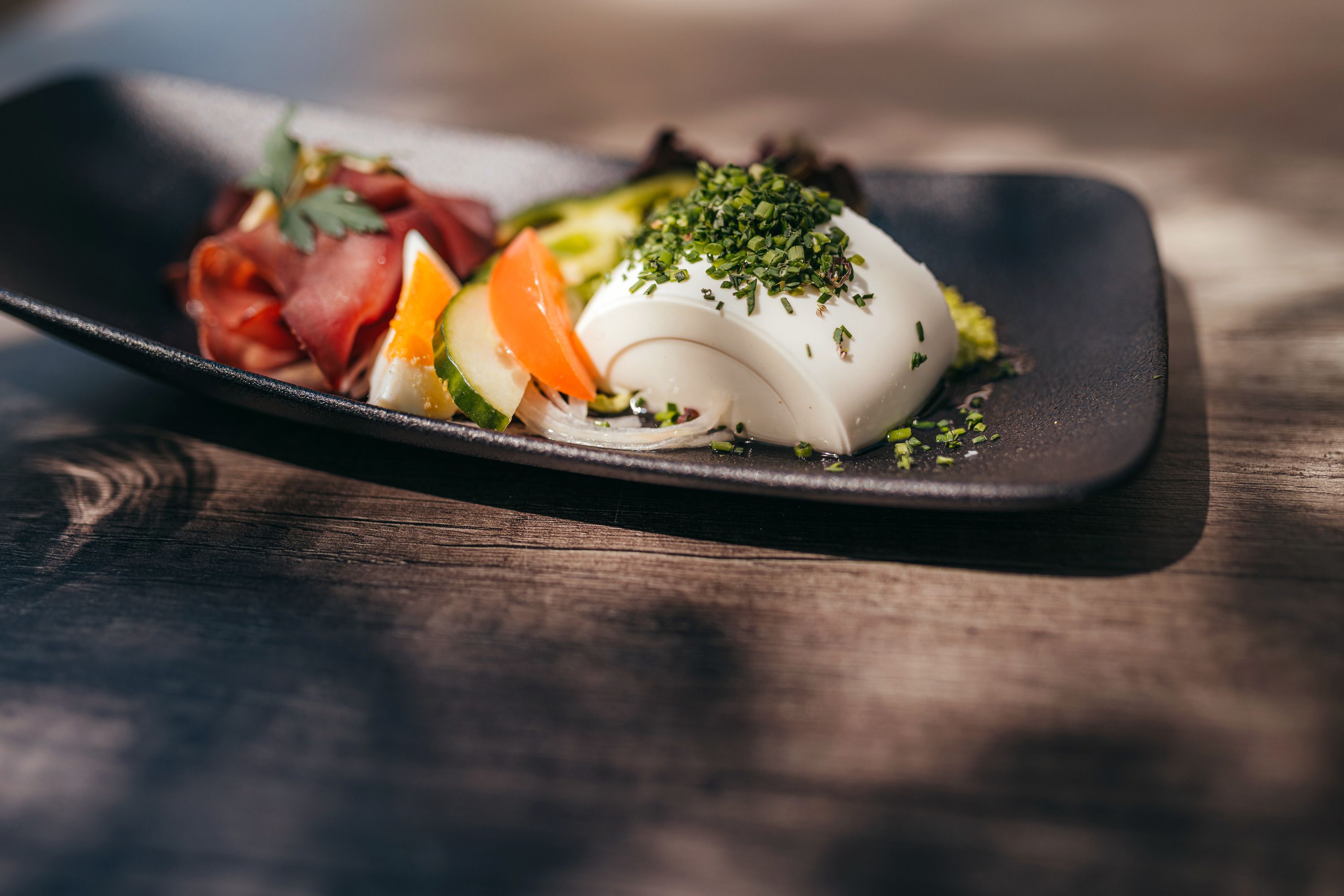 A plate of raw venison ham and vegetables, garnished with herbs.