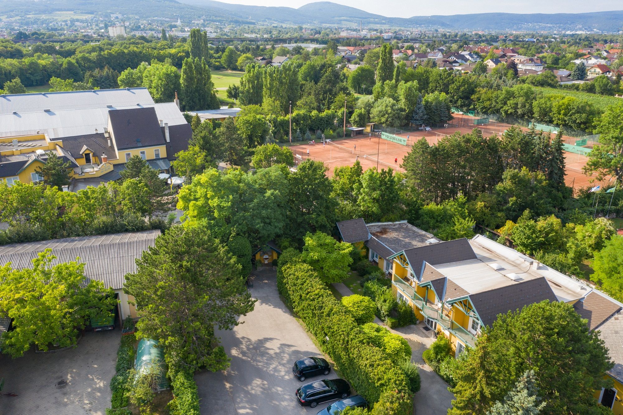 Aerial view of a tennis court with surrounding buildings and trees.
