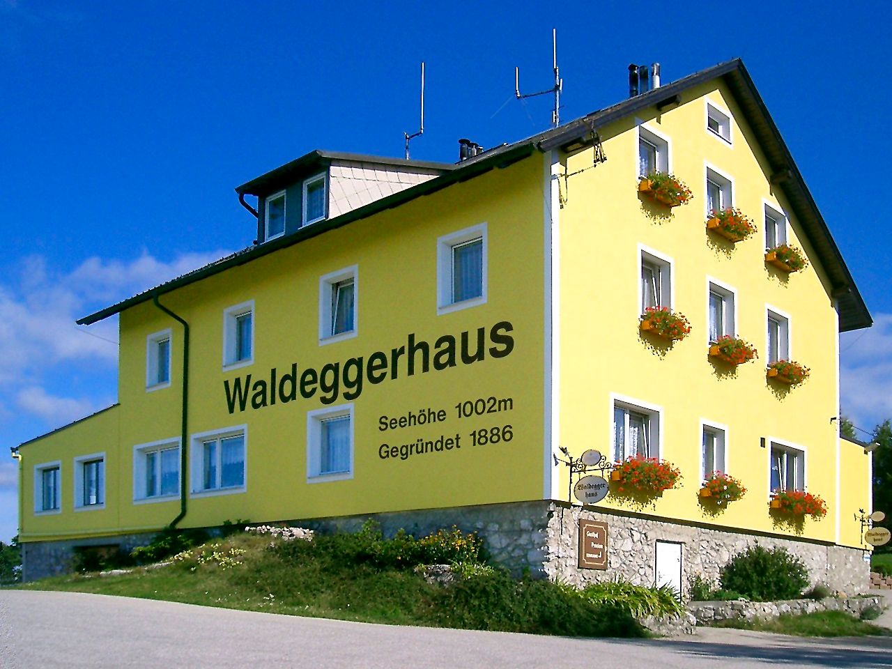 Yellow building with the inscription 'Waldeggerhaus', surrounded by flowers.