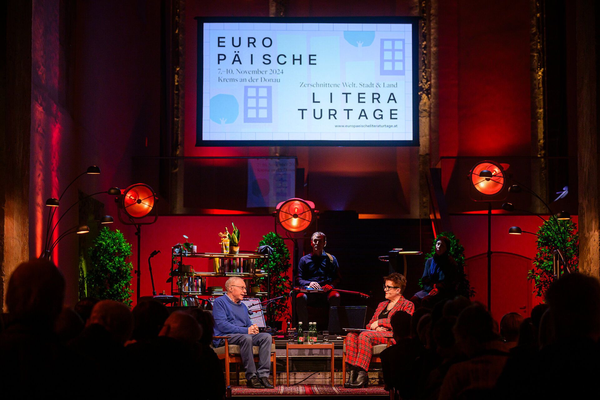 Podiumsgespräch auf einer Bühne bei den Europäischen Literaturtagen in Krems an der Donau, mit zwei Gesprächspartner:innen im Vordergrund und projiziertem Festival-Logo im Hintergrund.