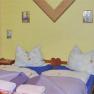Two single beds in a room with a yellow wall and decorative pictures.