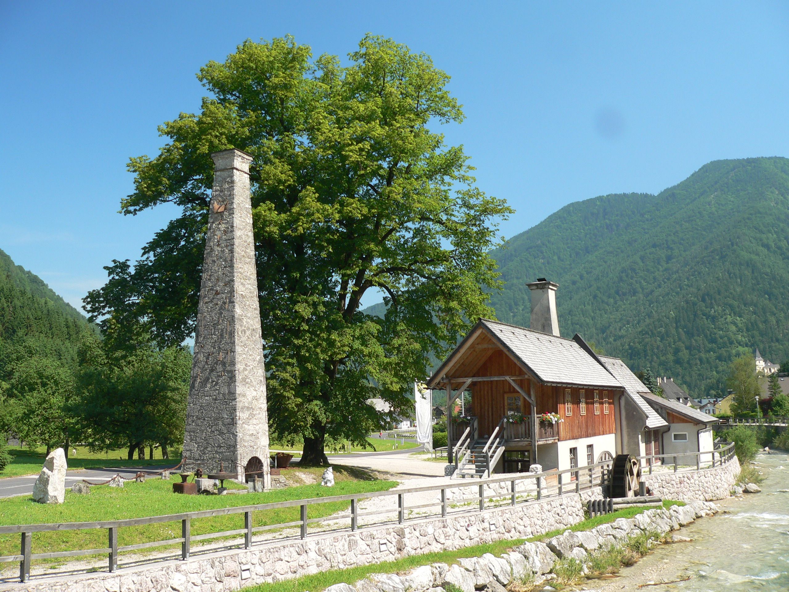 Historic building with chimney and water wheel in a rural setting.