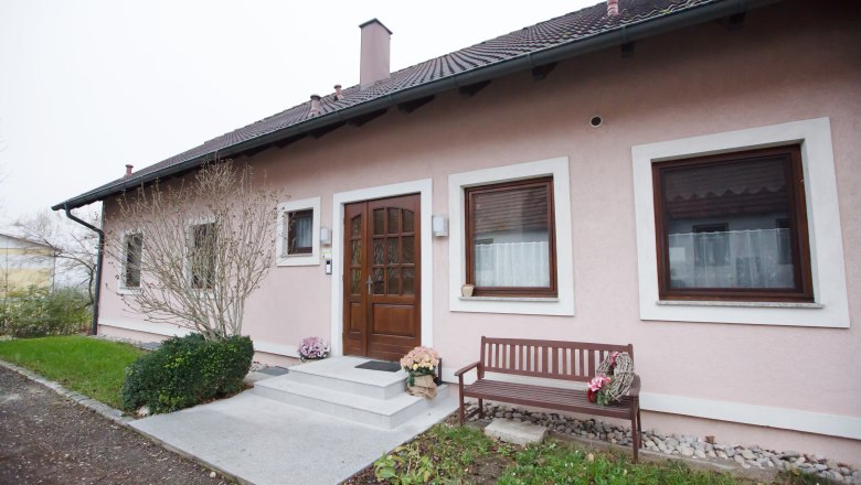 Vacation apartment Muck, © schwarz-könig.at Entrance to a pink-painted vacation apartment with a wooden door, two windows and a wooden bench next to it.