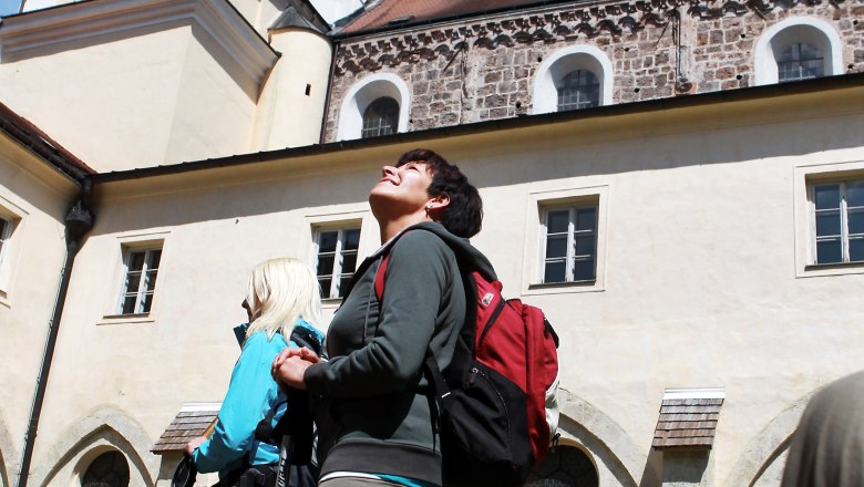 Two people with rucksacks and hiking poles stand in front of Lilienfeld Abbey and look up.
