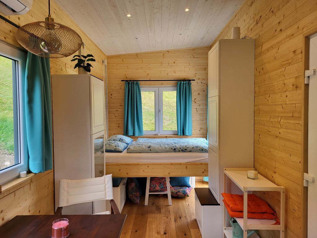 Small room with wooden walls, fold-down bed, blue curtains and shelves.