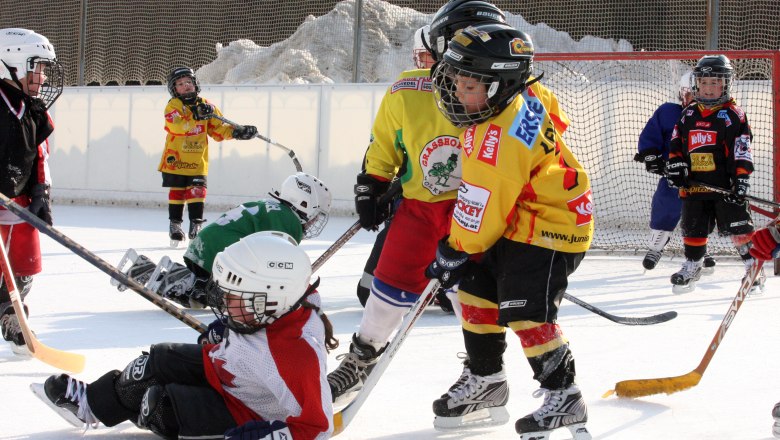 Children playing ice hockey on an outdoor rink.