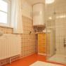 A bathroom with shower, washbasin, radiator and wooden cabinet. The walls are clad with patterned tiles.