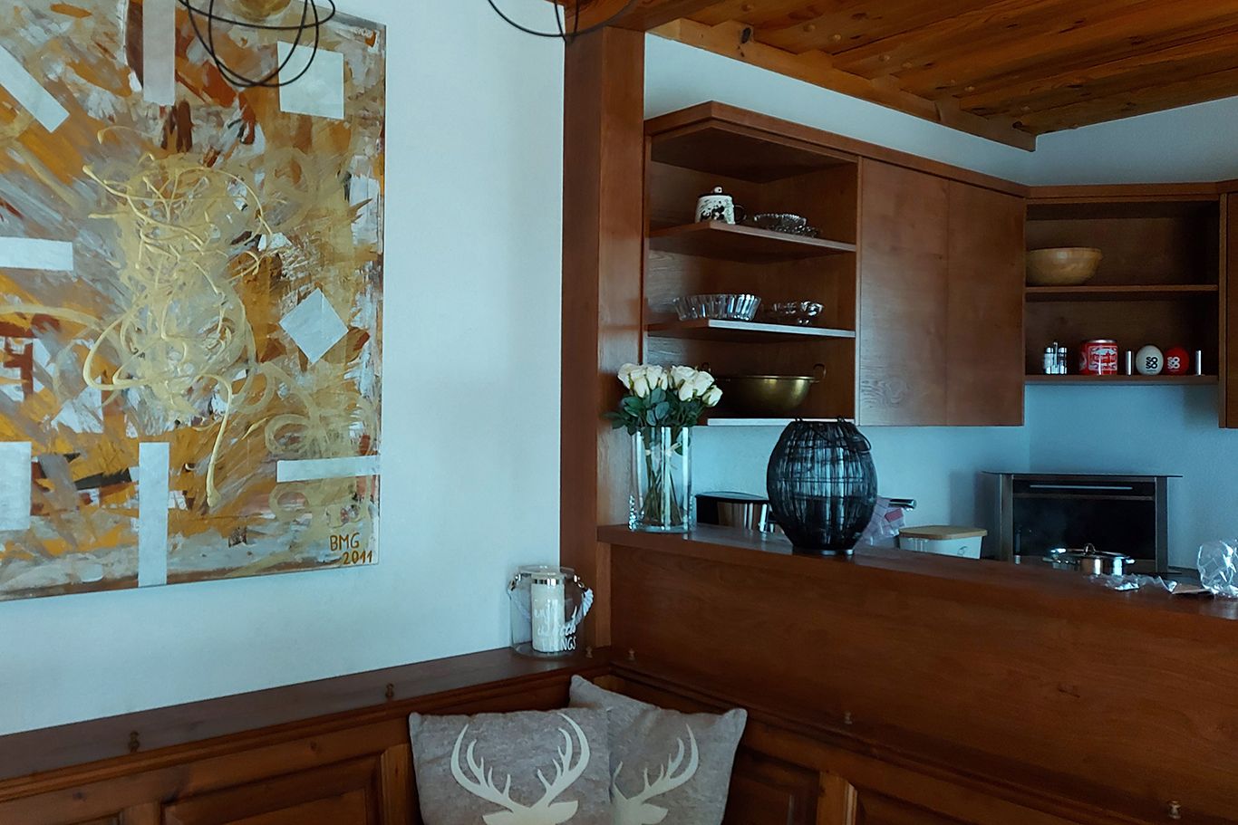 Wooden kitchen with artwork on the wall, vase with white roses and shelves with crockery.