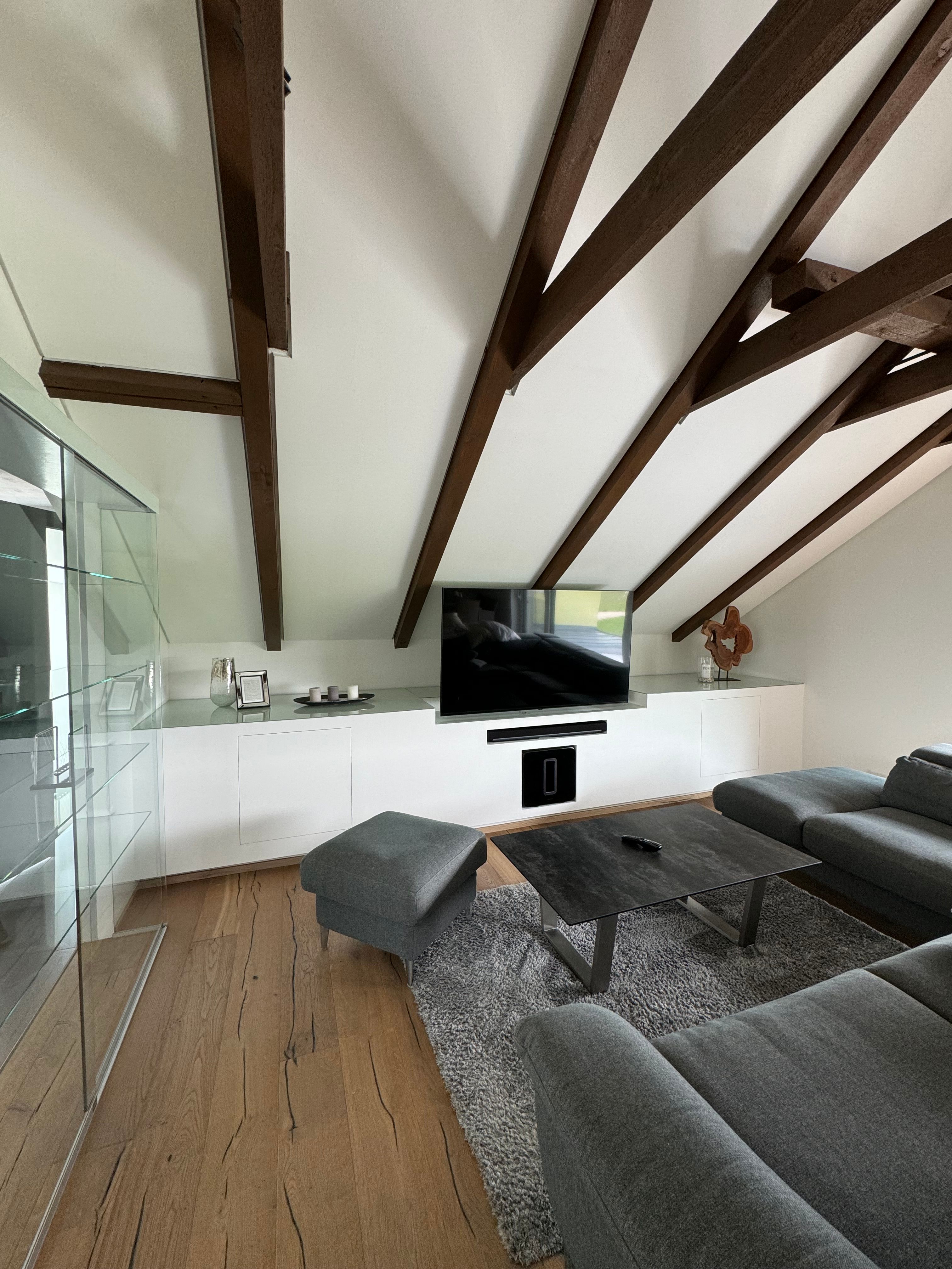 Modern living area with gray sofa, wooden beamed ceiling and flat screen TV.