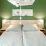Modern bedroom with green-painted wall, double bed and two bedside lamps.