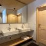 Modern bathroom with two washbasins, wooden ceiling and doors.