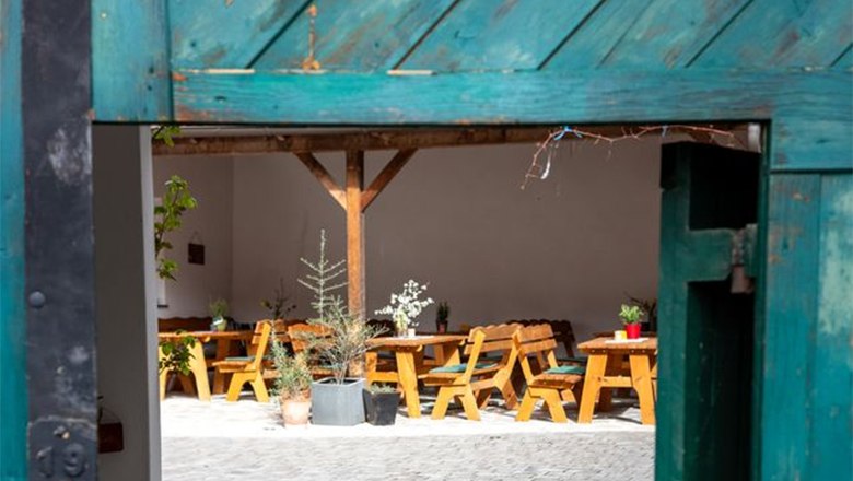 View through an open gate onto an inner courtyard with wooden tables and plants.