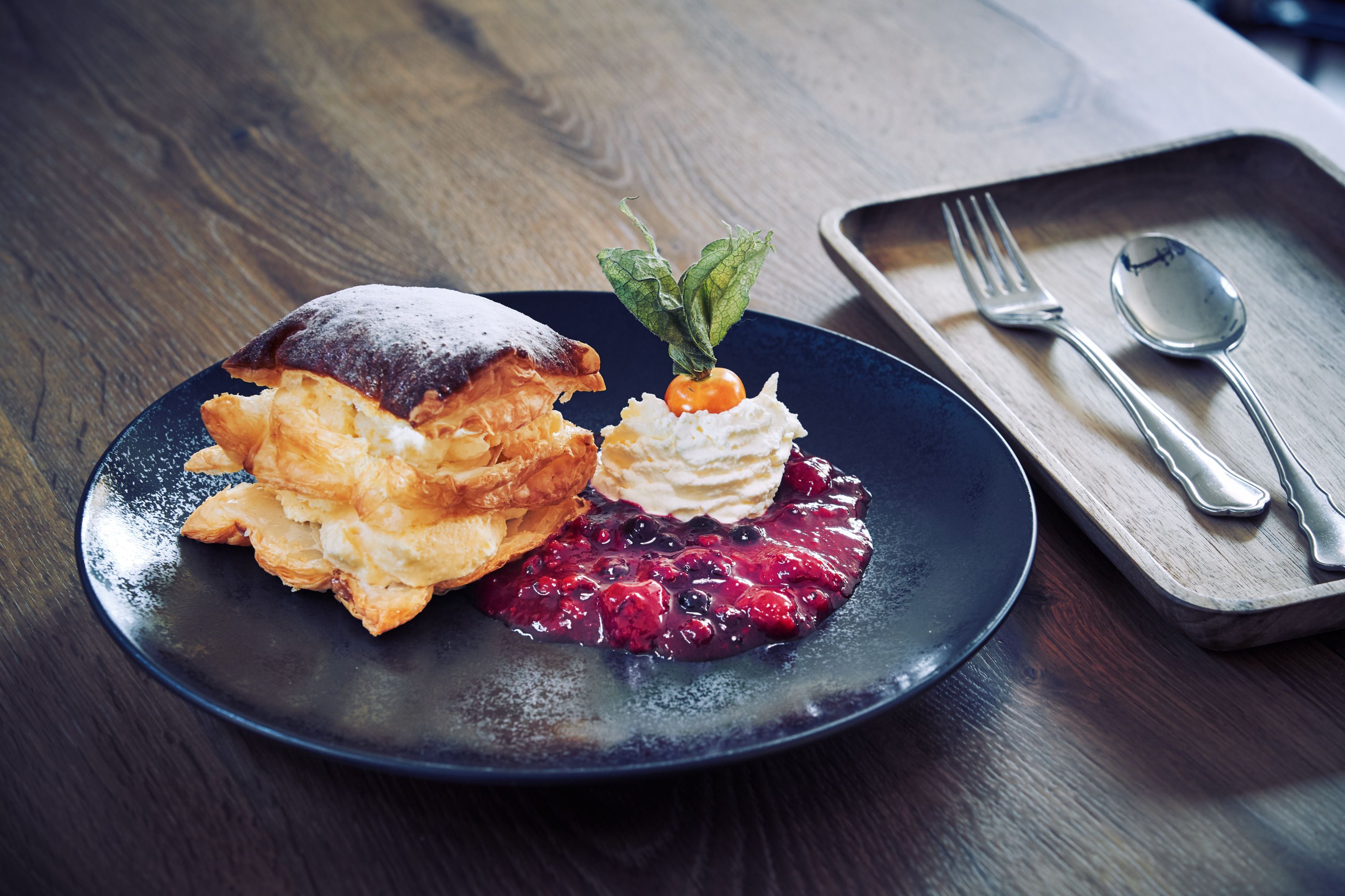 A dessert plate with a cream slice, roasted berries and whipped cream on a wooden table.