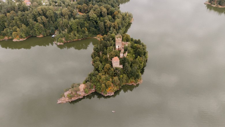 Aerial view of a castle ruin on a wooded island in a lake.