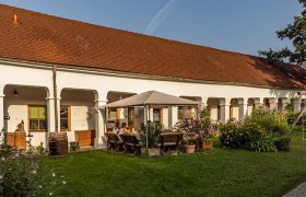 A traditional winery with white arcades, a red tiled roof and a garden with a seating area and flowers.