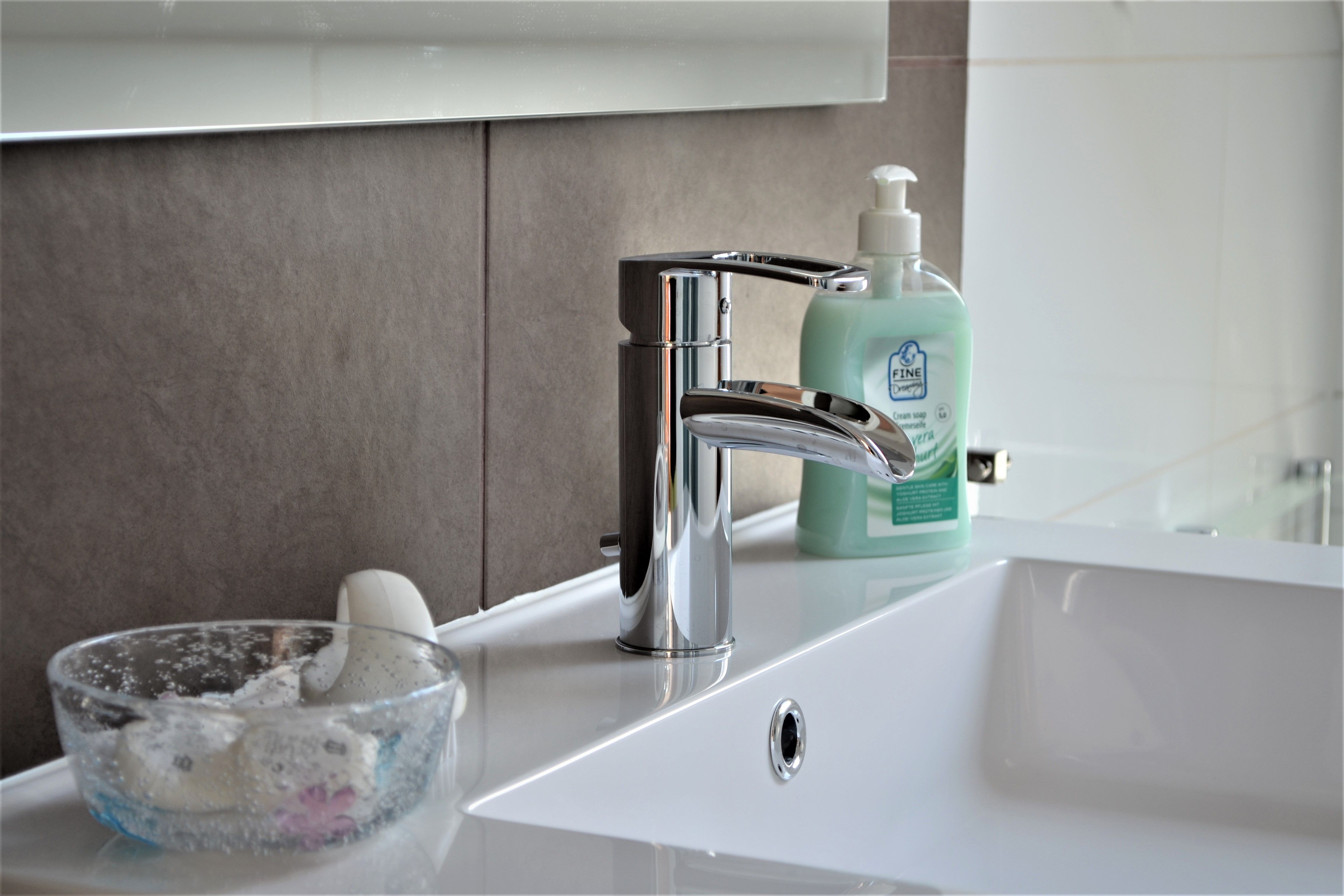 Close-up of a washbasin with soap dispenser and glass with soap.