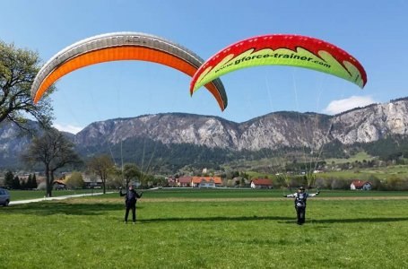 Two people practicing paragliding on a meadow in front of a mountain landscape.