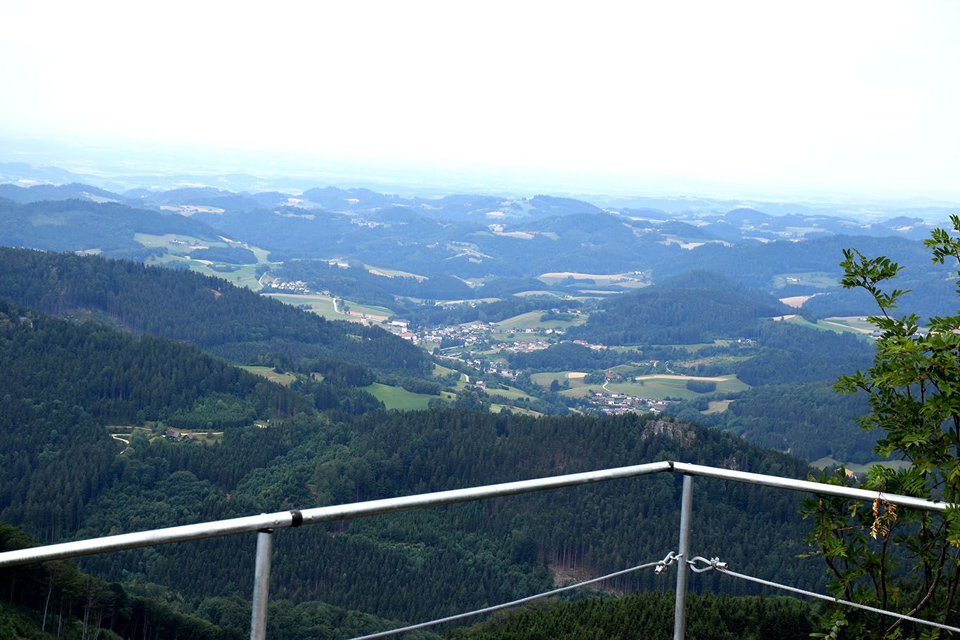 View from the castle stone wall of a hilly landscape with forests and villages.