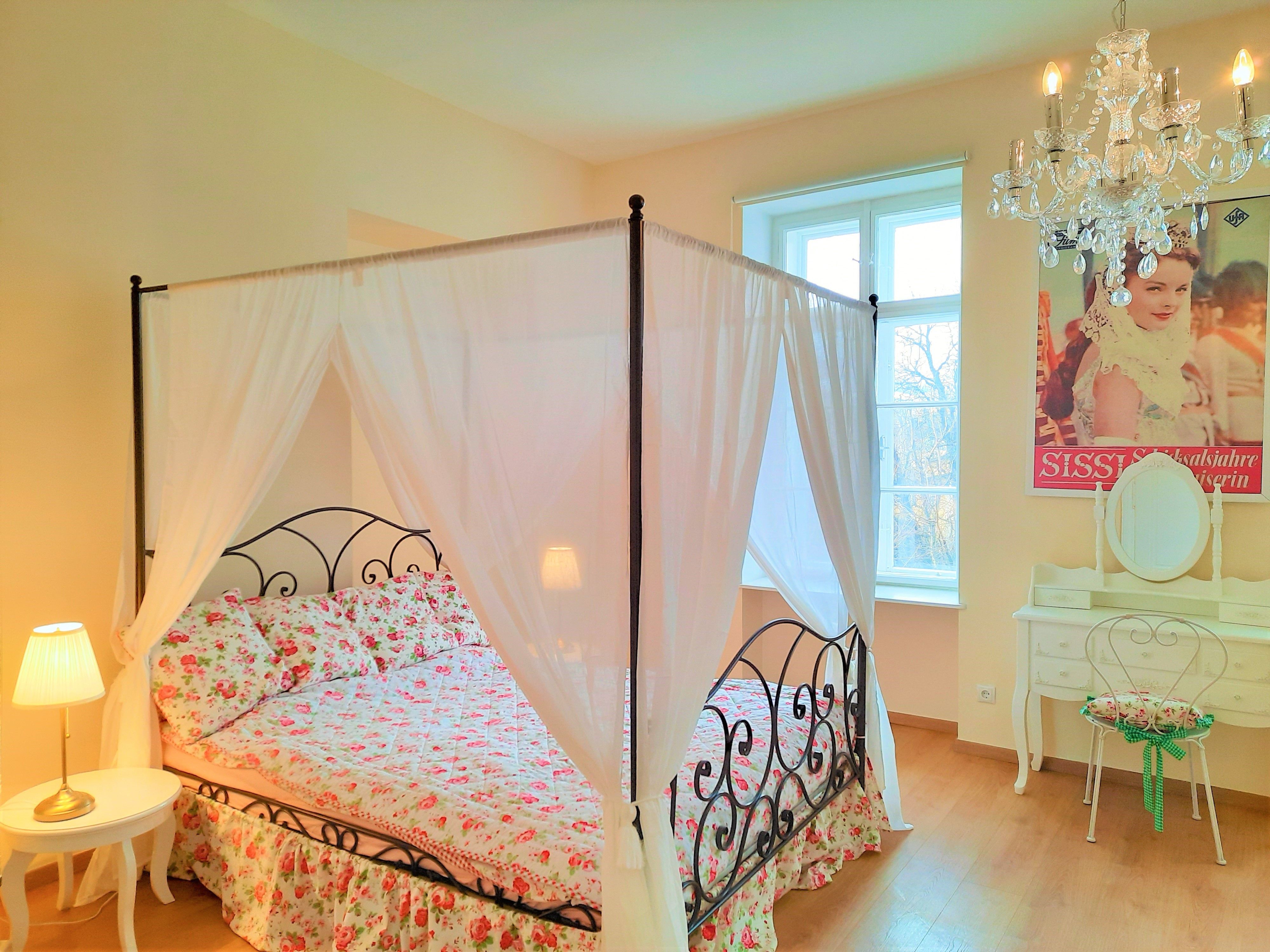 Bedroom with four-poster bed, floral bedding, chandelier and dressing table.