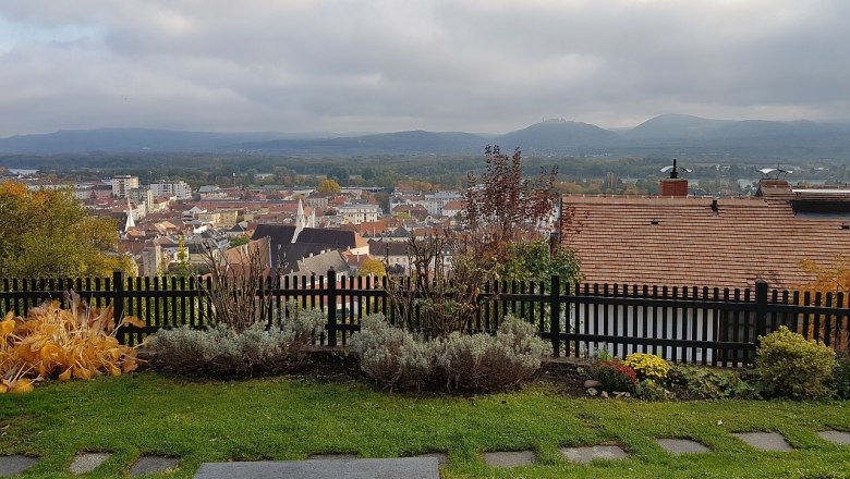 View over the town of Krems with houses, hills and a cloudy sky in the background.