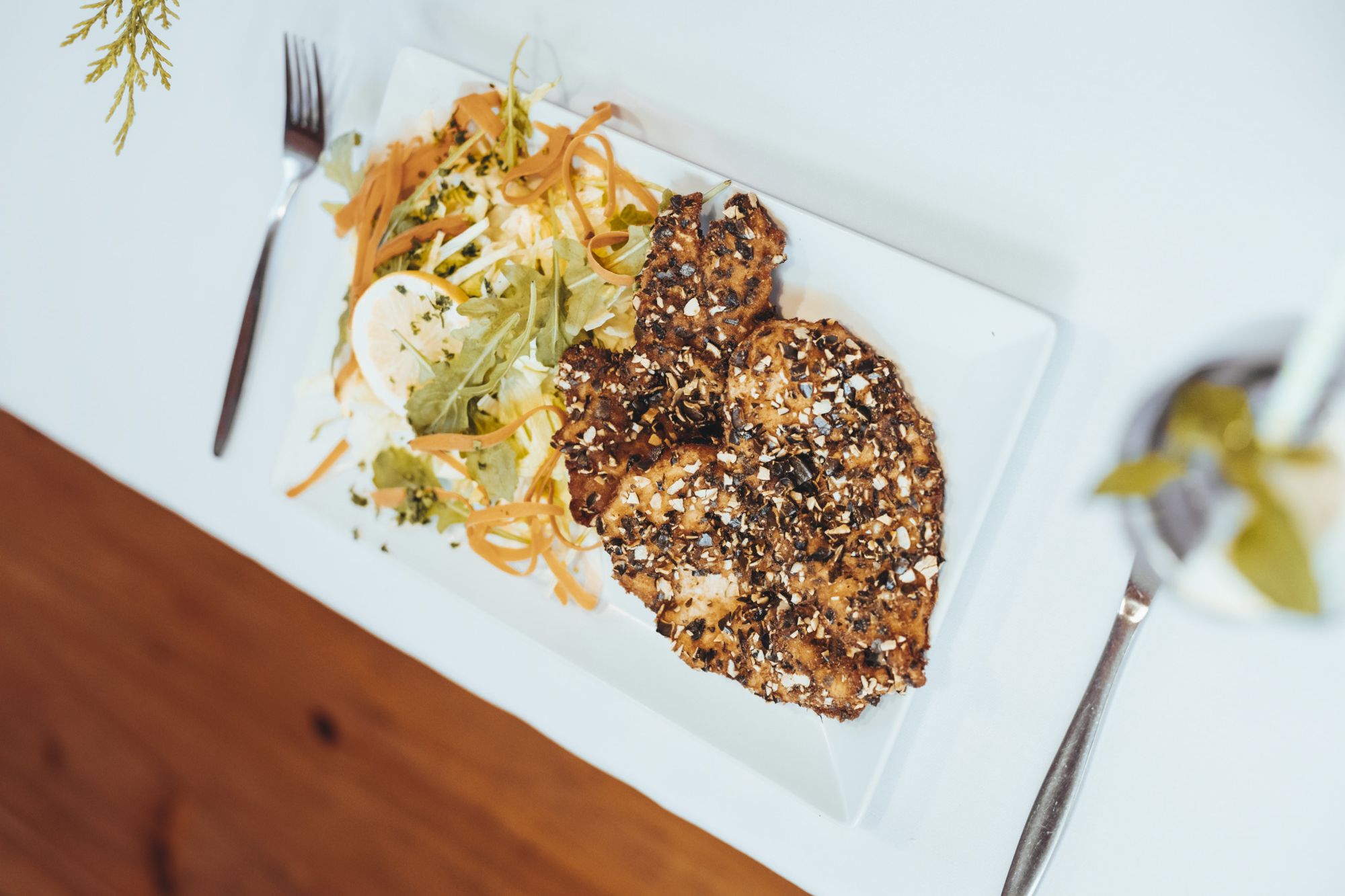 Chicken schnitzel with pumpkin seed breading and salad on a white plate.