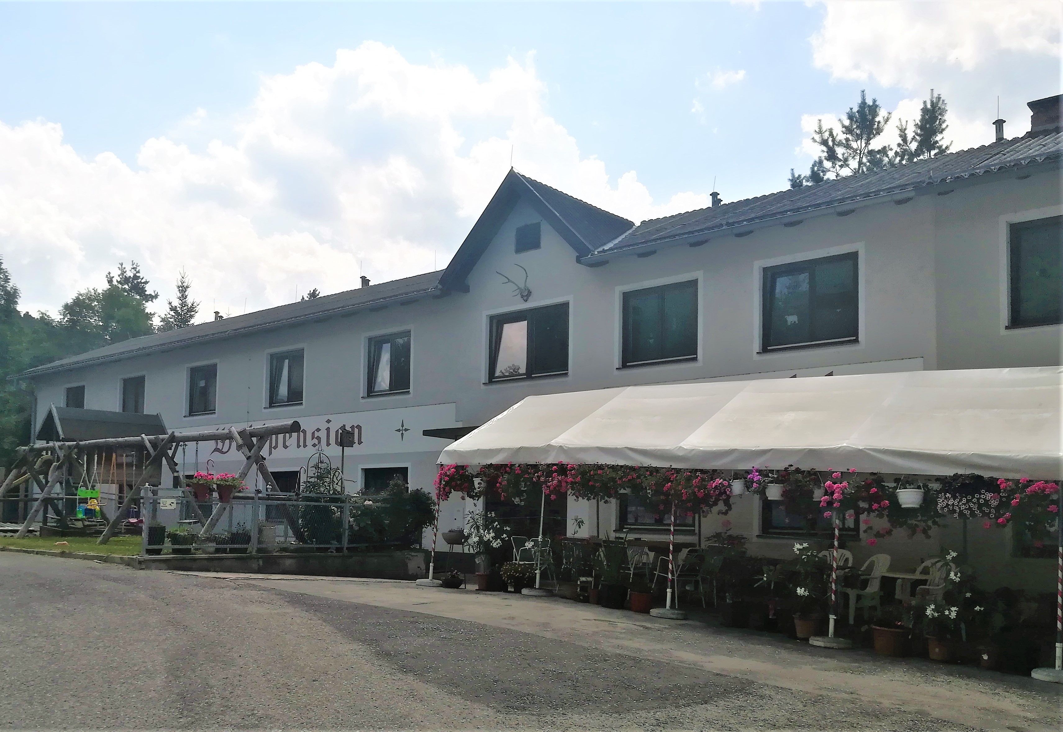 A two-storey building with the inscription 'Waldpension', surrounded by flowers and a canopy.