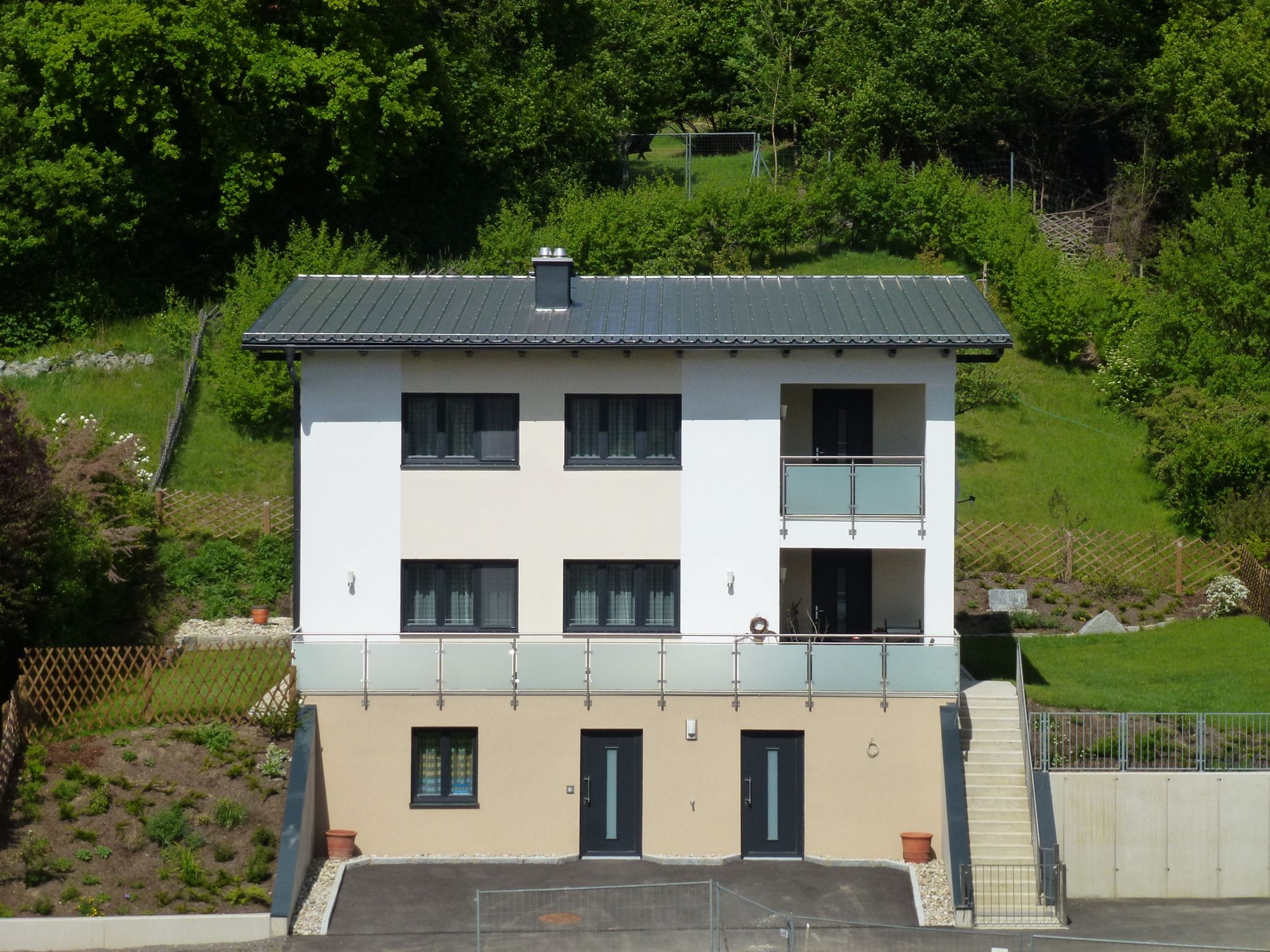 Two-storey modern house with balcony, surrounded by green countryside.