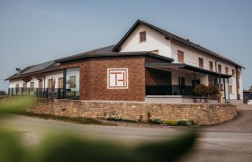 A modern building with the inscription 'Gasthof Thaler', surrounded by a stone wall and plants.