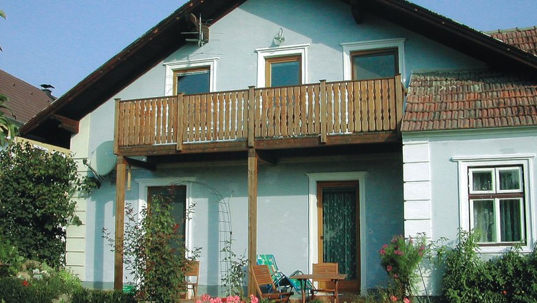 A traditional winegrower's house with a wooden balcony and garden furniture in front of the door.