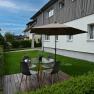Garden with seating area, table, chairs and parasol on wooden terrace.