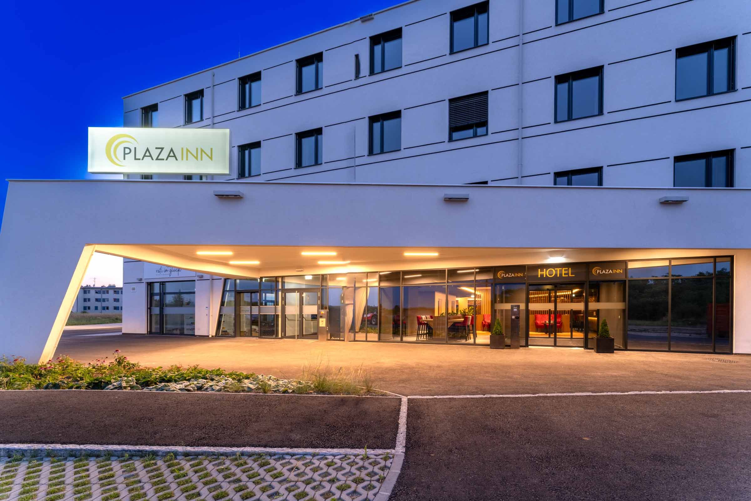 Entrance to the Plaza Inn Hotel at night with illuminated sign and modern architecture.
