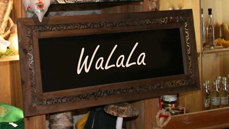 A decorative wooden sign with the inscription 'WaLaLa' in a rustic store with shelves full of products.