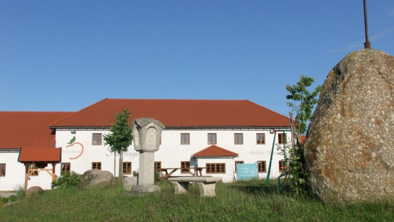 A farm with a red roof and a large stone with a cross in the foreground.