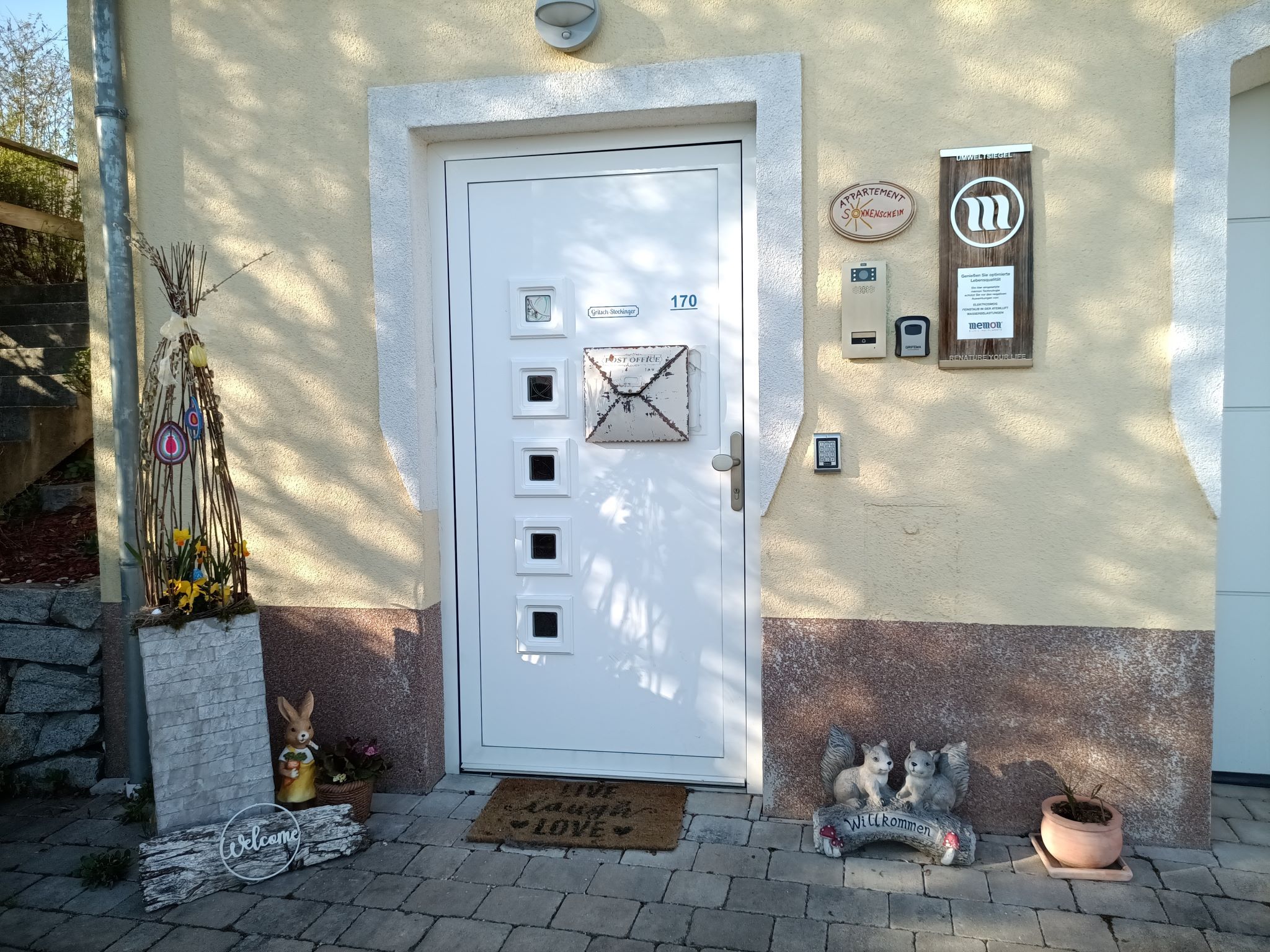 Entrance area of a house with decorative elements such as a rabbit, a welcome sign and flowers.